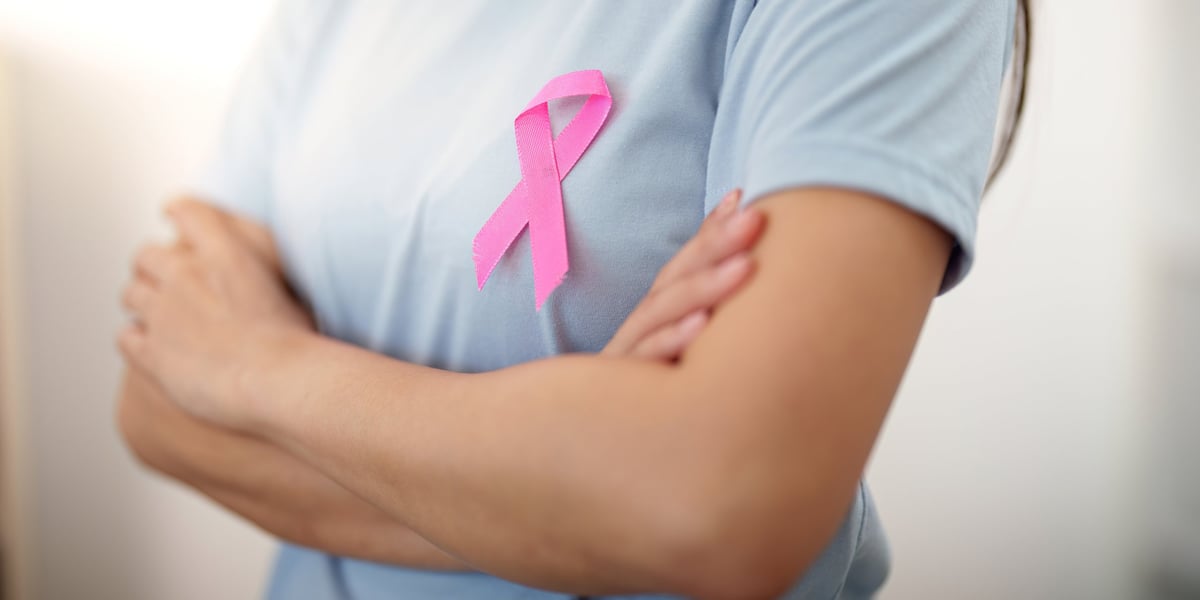 A woman proudly showcases a pink ribbon on her shirt, symbolizing breast cancer awareness and support for those affected.