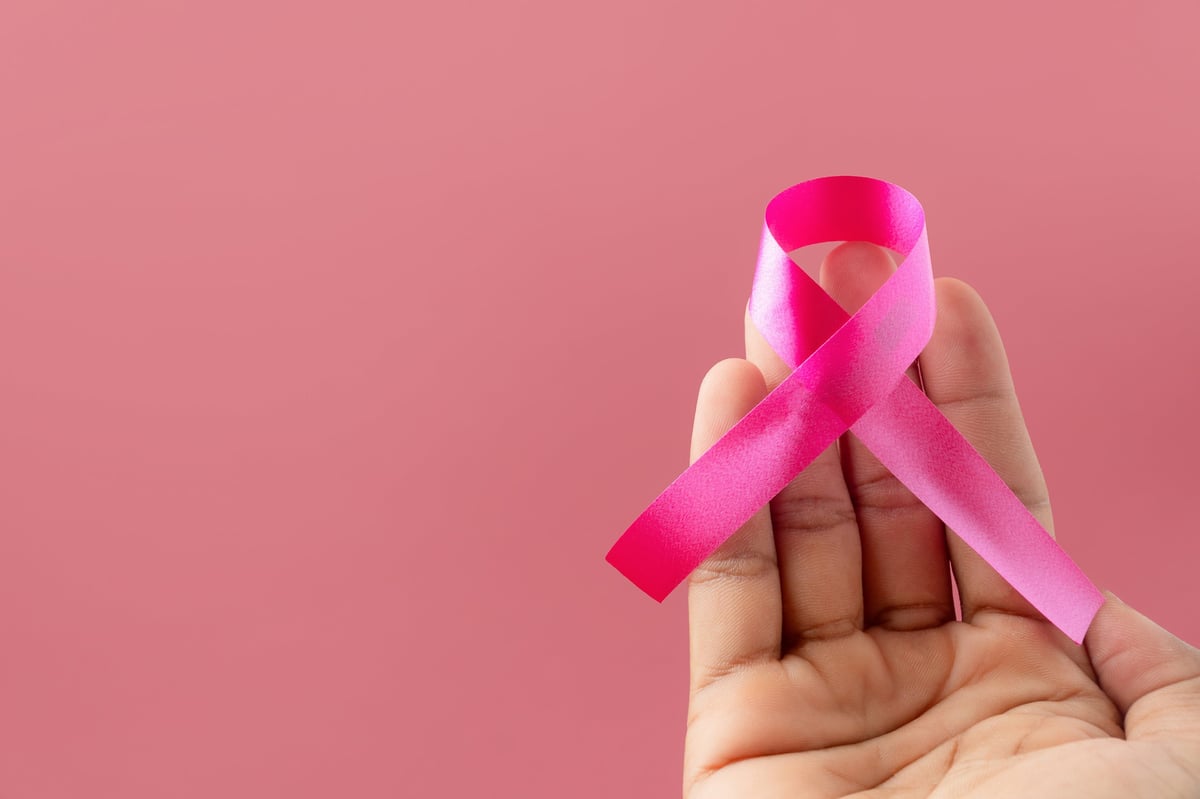 Hand holding a pink ribbon, representing breast cancer prevention and support